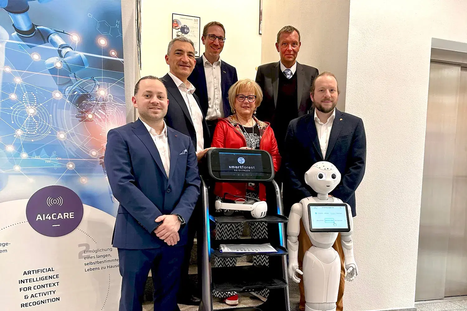 Gruppenbild mit sechs Personen auf einer Treppe, davor ein Transportroboter mit dem Logo von SMART FOREST 5G Clinics auf dem Display und ein humanoider Roboter mit Tablet